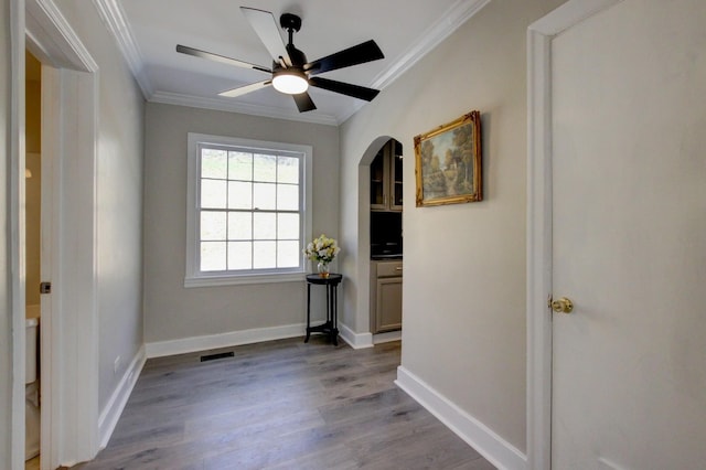 interior space with a ceiling fan, baseboards, wood finished floors, visible vents, and ornamental molding