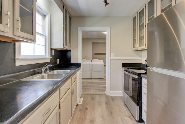kitchen with a sink, light wood-style floors, appliances with stainless steel finishes, dark countertops, and washing machine and dryer