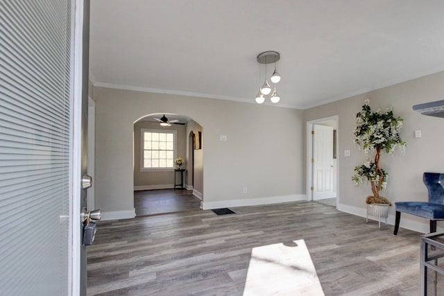 foyer featuring arched walkways, crown molding, baseboards, and wood finished floors