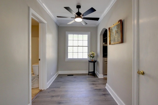 corridor with crown molding, dark wood-style floors, baseboards, and arched walkways
