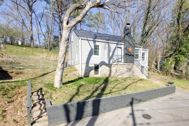 view of front facade with metal roof, a front yard, a chimney, and fence