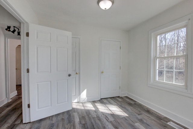 unfurnished bedroom with visible vents, wood finished floors, baseboards, and arched walkways