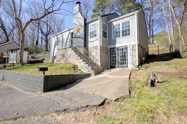 view of front facade featuring an outbuilding, fence, french doors, a front yard, and a chimney