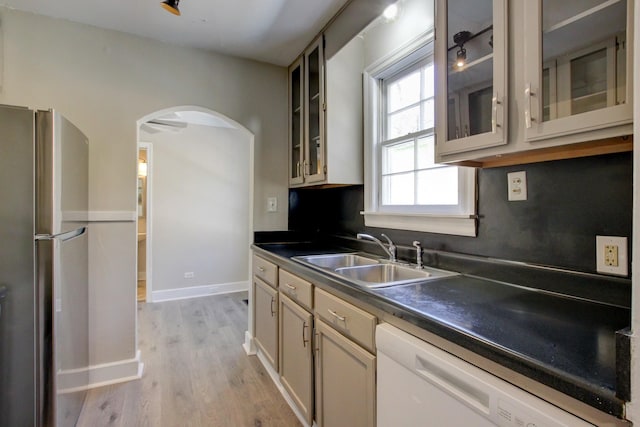 kitchen featuring a sink, tasteful backsplash, freestanding refrigerator, arched walkways, and white dishwasher