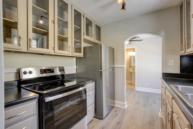 kitchen featuring dark countertops, cream cabinets, arched walkways, appliances with stainless steel finishes, and light wood finished floors