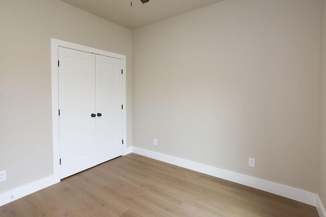 unfurnished bedroom featuring light wood-style floors, baseboards, and a closet