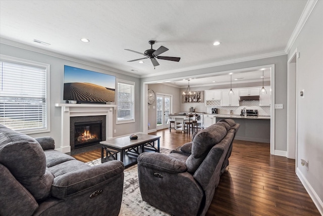 living room featuring a ceiling fan, visible vents, a fireplace with flush hearth, dark wood-type flooring, and crown molding