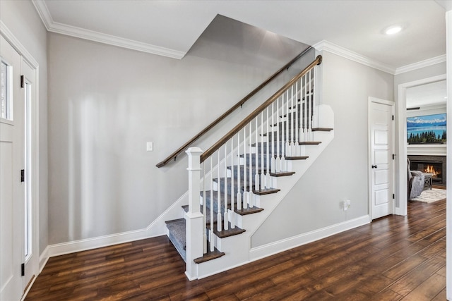 stairway featuring a glass covered fireplace, wood finished floors, baseboards, and ornamental molding