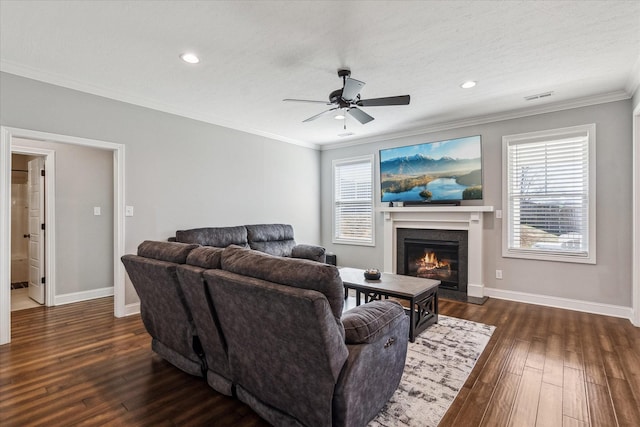 living area with a ceiling fan, baseboards, a fireplace with flush hearth, dark wood-style flooring, and crown molding