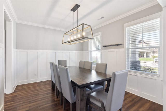 dining area featuring visible vents, crown molding, an inviting chandelier, a decorative wall, and dark wood-style flooring