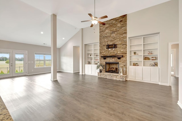 unfurnished living room featuring wood finished floors, a stone fireplace, baseboards, and ceiling fan