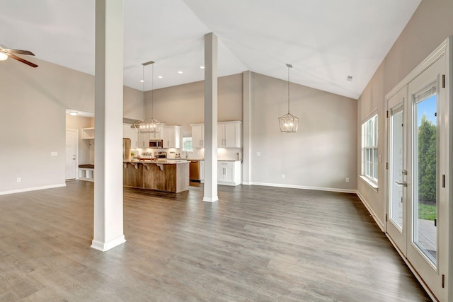 unfurnished living room featuring dark wood-type flooring, high vaulted ceiling, baseboards, and ceiling fan with notable chandelier