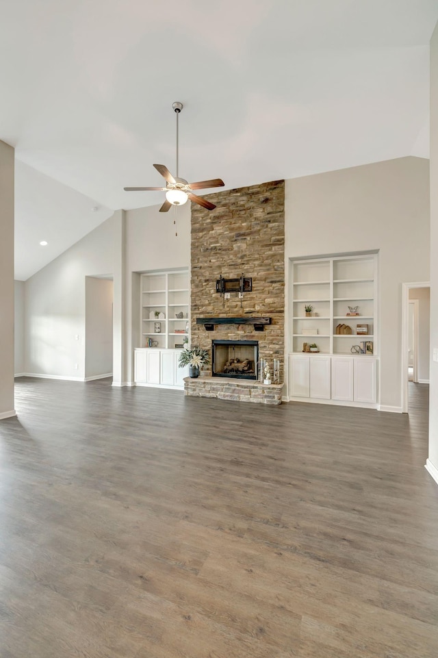 unfurnished living room with baseboards, built in shelves, ceiling fan, a stone fireplace, and wood finished floors