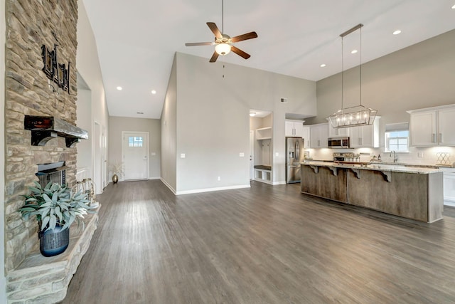 unfurnished living room with dark wood finished floors, a stone fireplace, ceiling fan, and a sink