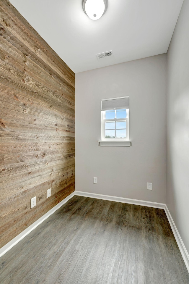 unfurnished room with baseboards, visible vents, wooden walls, and wood finished floors