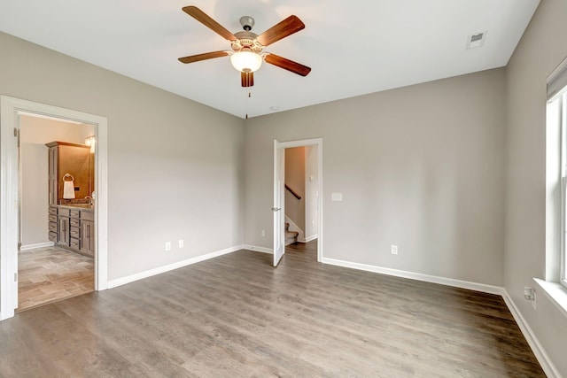 unfurnished bedroom featuring wood finished floors, ensuite bathroom, baseboards, visible vents, and ceiling fan