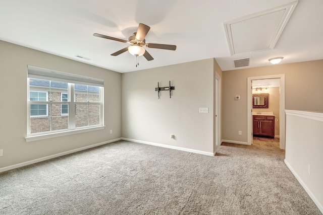 carpeted empty room with attic access, baseboards, visible vents, and ceiling fan