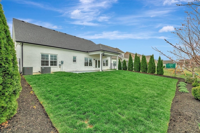 rear view of property featuring roof with shingles, central air condition unit, a fenced backyard, ceiling fan, and a yard