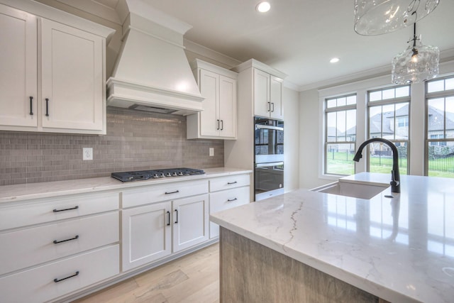 1251 Payton Ln, Gallatin, TN 37066 - kitchen featuring stainless steel gas cooktop, ornamental molding, custom exhaust hood, light wood-style flooring, and a sink