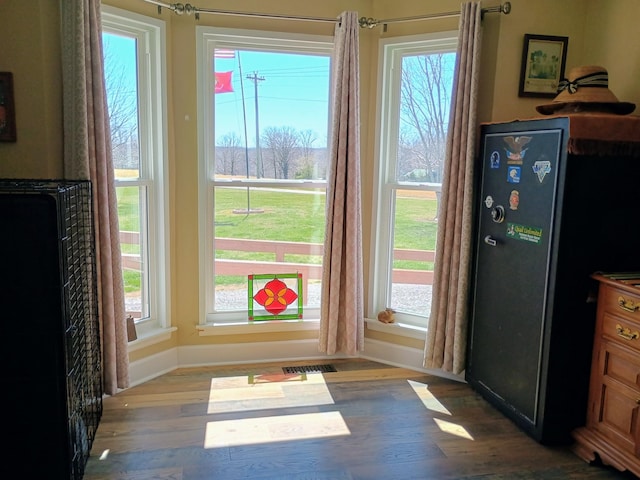 doorway with baseboards, wood finished floors, visible vents, and plenty of natural light