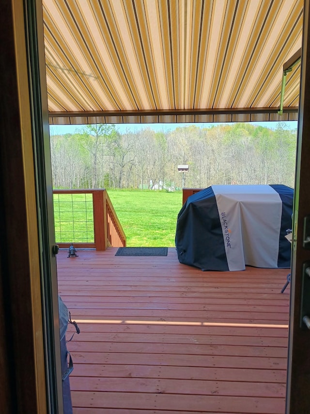 deck with grilling area, a forest view, and a yard
