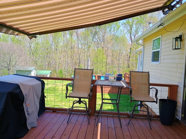 wooden deck with a forest view, a lawn, and a grill