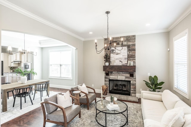living room featuring dark wood-type flooring, ornamental molding, arched walkways, an inviting chandelier, and baseboards
