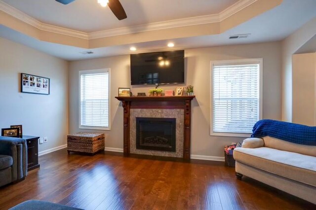 living area with wood-type flooring, visible vents, a raised ceiling, and ornamental molding