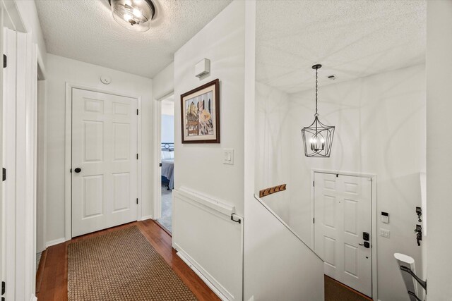 corridor featuring an inviting chandelier, dark wood-type flooring, baseboards, and a textured ceiling