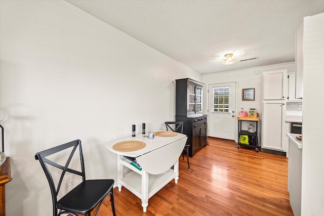 dining area with light wood-style flooring, a textured ceiling, and visible vents