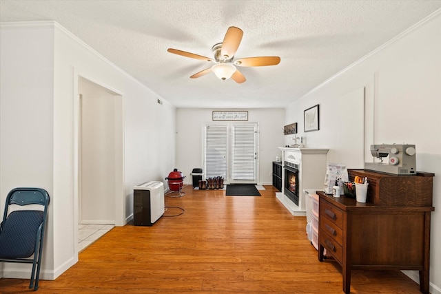 entrance foyer with a warm lit fireplace, a textured ceiling, light wood-style floors, ceiling fan, and ornamental molding