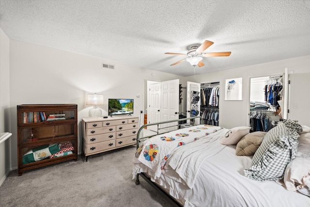 bedroom with multiple closets, a textured ceiling, ceiling fan, visible vents, and light carpet