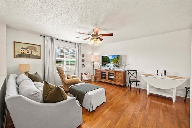 living area with hardwood / wood-style flooring, a textured ceiling, baseboards, visible vents, and ceiling fan