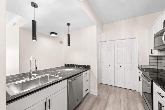 kitchen featuring dark countertops, light wood finished floors, tasteful backsplash, stainless steel appliances, and a sink