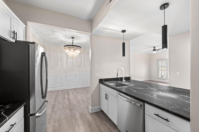 kitchen featuring light wood-type flooring, ceiling fan with notable chandelier, a sink, stainless steel appliances, and white cabinets