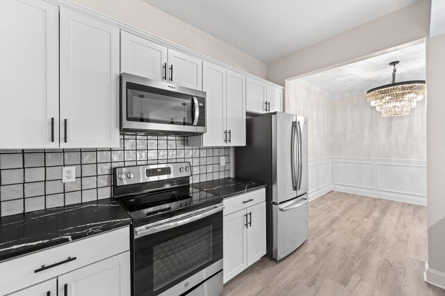 kitchen featuring backsplash, appliances with stainless steel finishes, light wood-style floors, a notable chandelier, and white cabinets