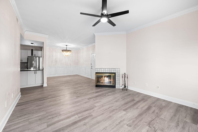 unfurnished living room featuring ceiling fan with notable chandelier, a tile fireplace, crown molding, and wood finished floors