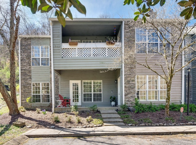 view of front of property featuring stone siding, a balcony, and a porch