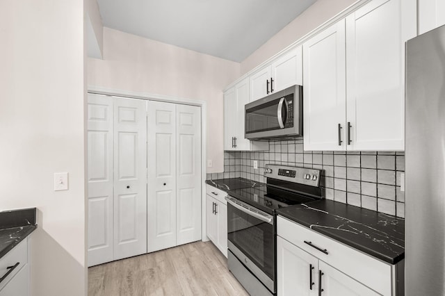 kitchen featuring dark countertops, white cabinetry, stainless steel appliances, and light wood-type flooring