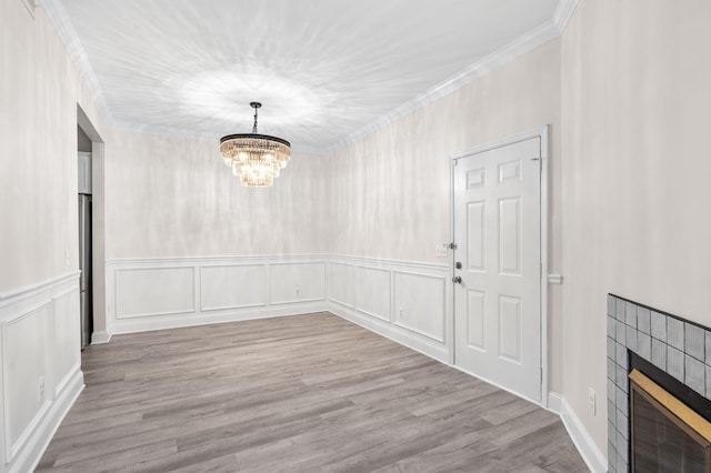unfurnished dining area featuring wood finished floors, a fireplace, crown molding, a decorative wall, and a notable chandelier