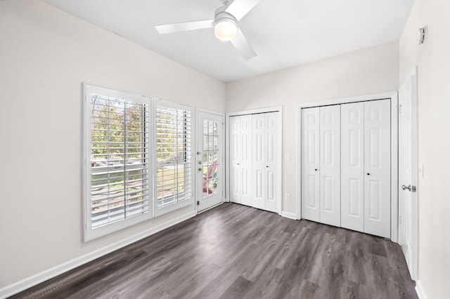 unfurnished bedroom featuring two closets, a ceiling fan, access to outside, dark wood finished floors, and baseboards