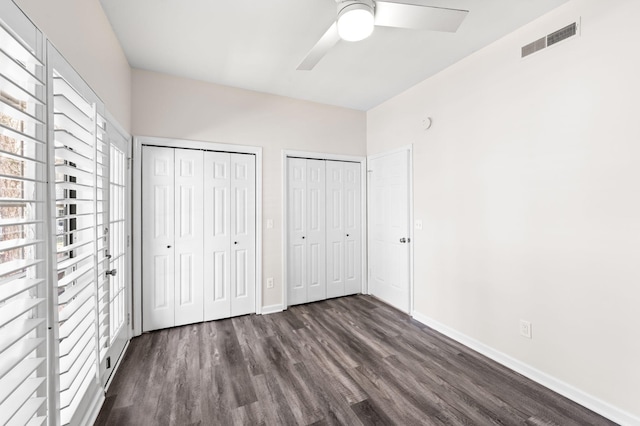 unfurnished bedroom with a ceiling fan, baseboards, visible vents, dark wood finished floors, and two closets