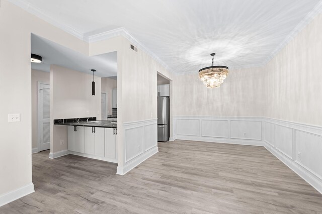 interior space featuring visible vents, light wood-style flooring, ornamental molding, a decorative wall, and a chandelier