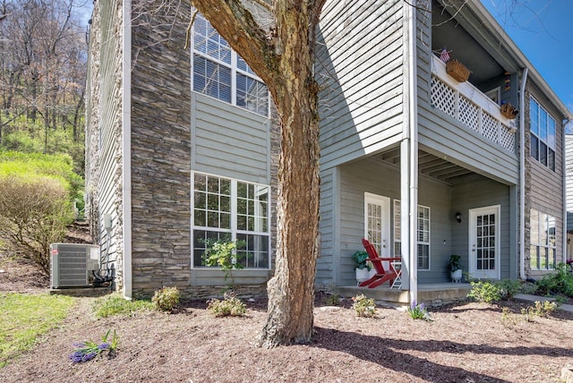 view of side of home featuring cooling unit, stone siding, and a balcony