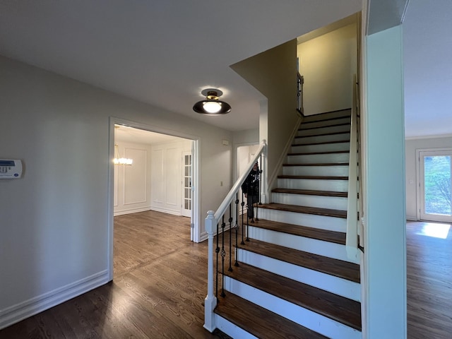 staircase featuring baseboards, a notable chandelier, and wood finished floors