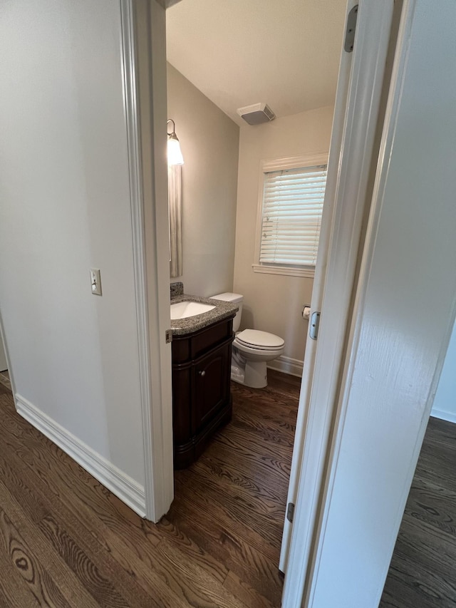 half bath with vanity, baseboards, toilet, visible vents, and wood finished floors
