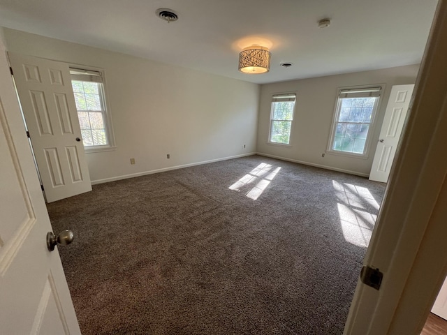 spare room featuring dark carpet, visible vents, and baseboards