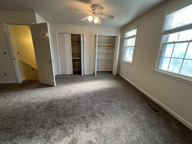 unfurnished bedroom featuring visible vents, baseboards, carpet, and two closets