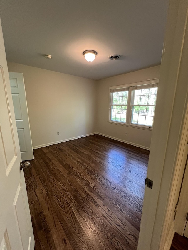 empty room featuring visible vents, baseboards, and dark wood finished floors