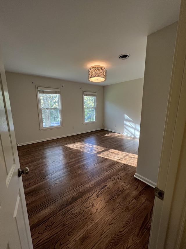empty room with visible vents, dark wood-style flooring, and baseboards